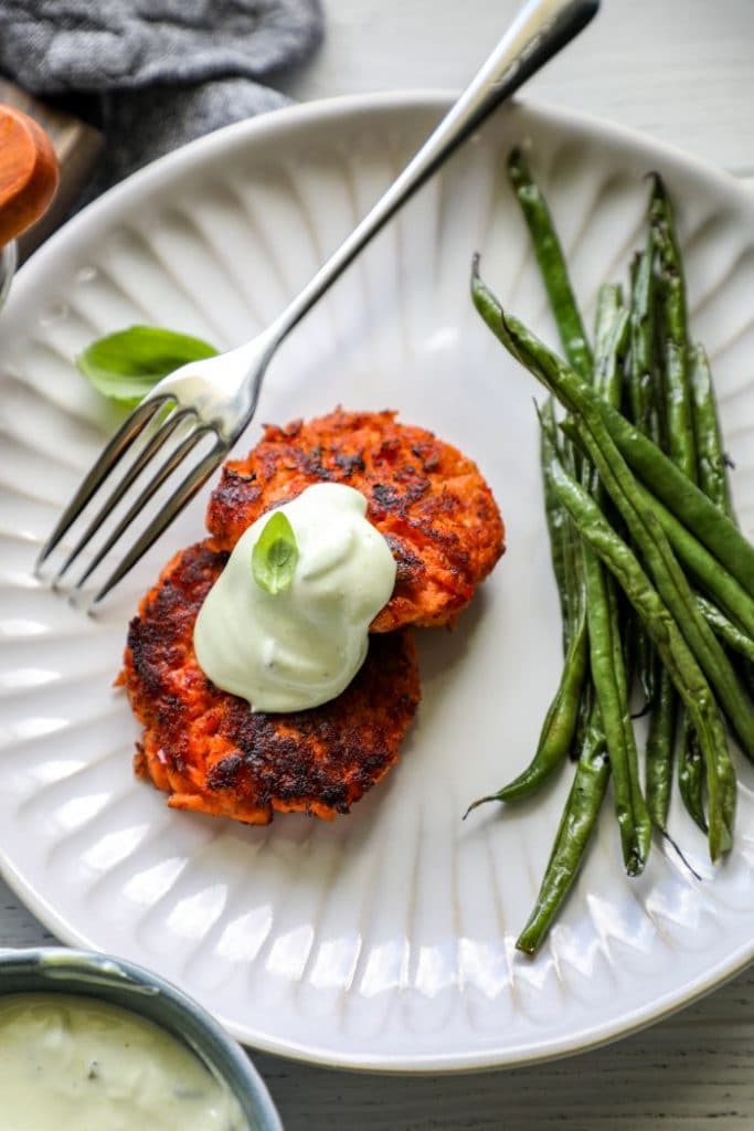 Two salmon cakes on a plate with sauce and green beans