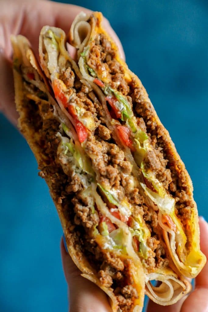 Two hands holding a keto crunchwrap with a blue background