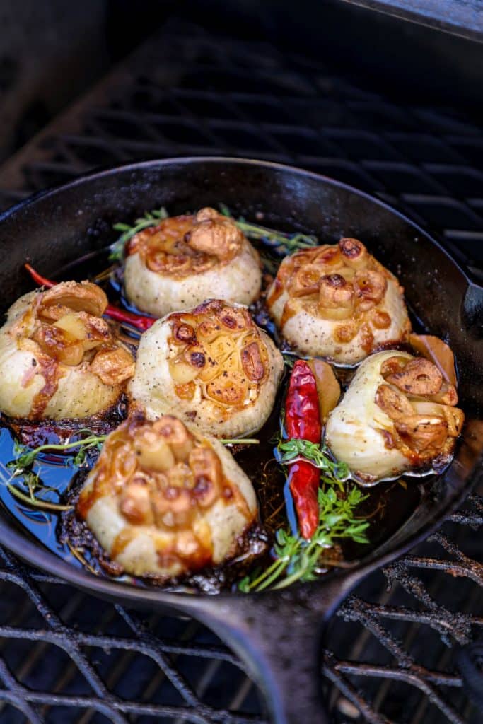 Smoked garlic confit in a cast iron pan on the grill