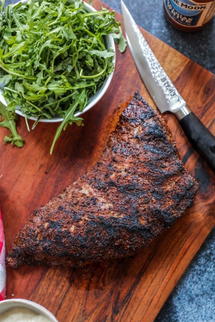 A whole tri tip on the cutting board with a knife.