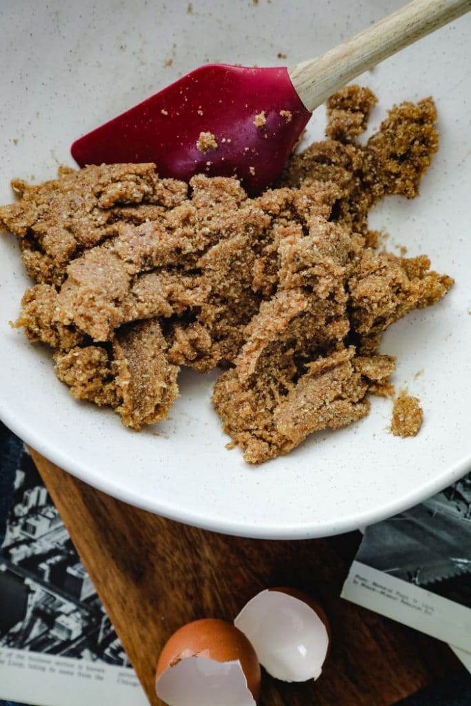 Keto graham cracker crust, mixed together in a white mixing bowl with a spatula