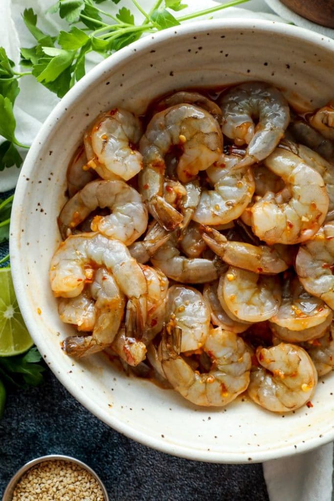 Shrimp coated in the chili sesame marinade in a white bowl.
