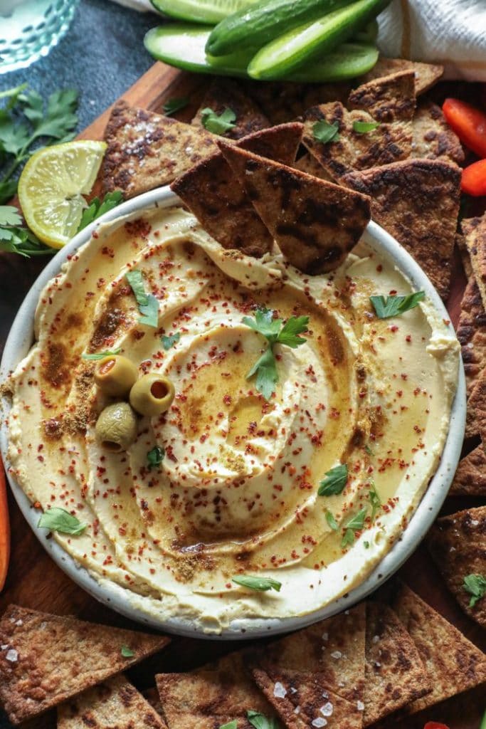 Two keto pita chips in a bowl of hummus with olives.