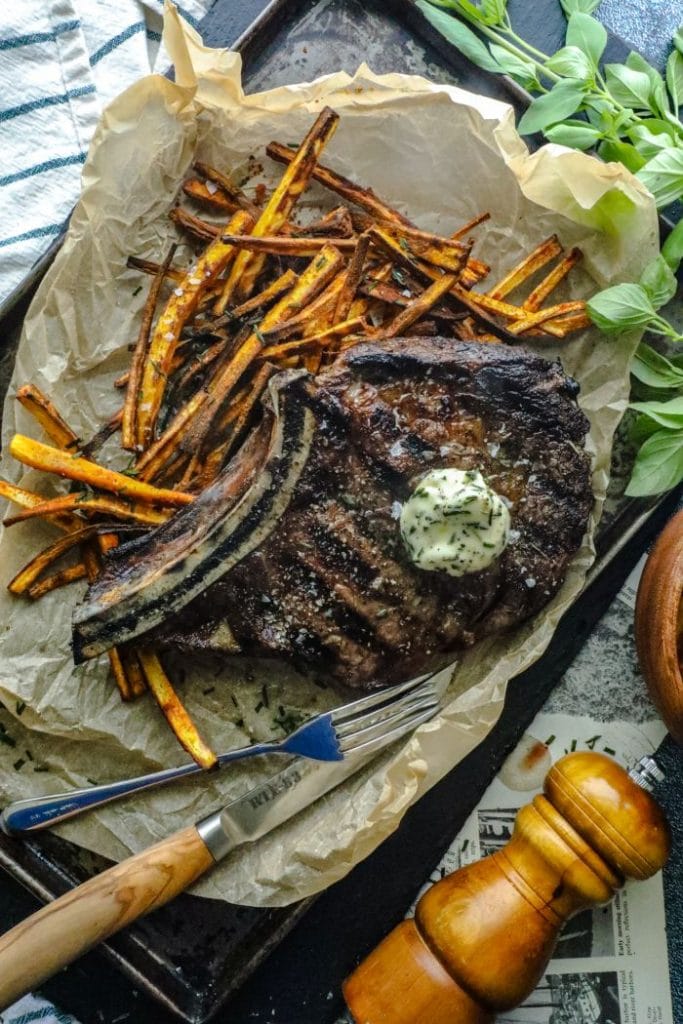Keto Steak Frites with a bone in ribeye over a bed of jicama fries on a tray.