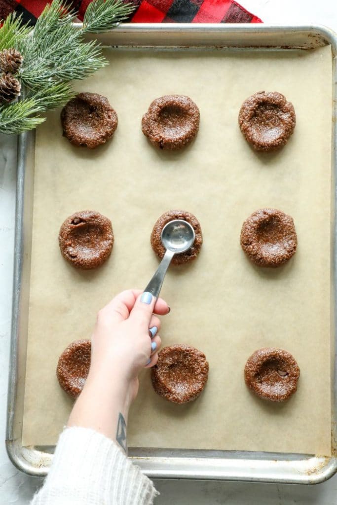 A spoon pressing into the center of a partially baked keto hot cocoa cookie.