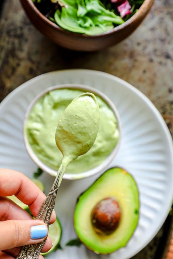 Spoon with avocado dressing on it over a bowl