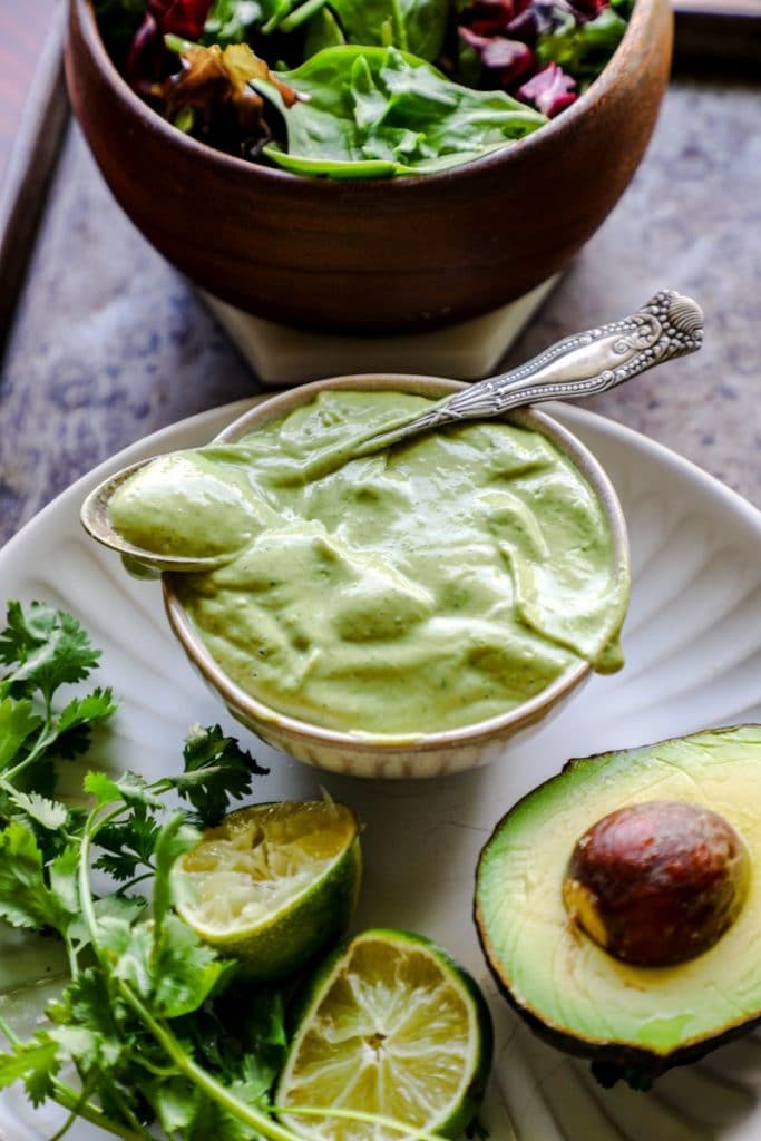 Avocado dressing with a spoon across a bowl on a black tray