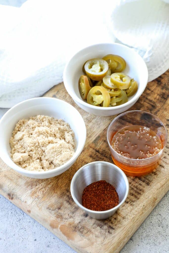 Brown sugar, jalapeños, honey and BBQ seasoning on a wooden cutting board.