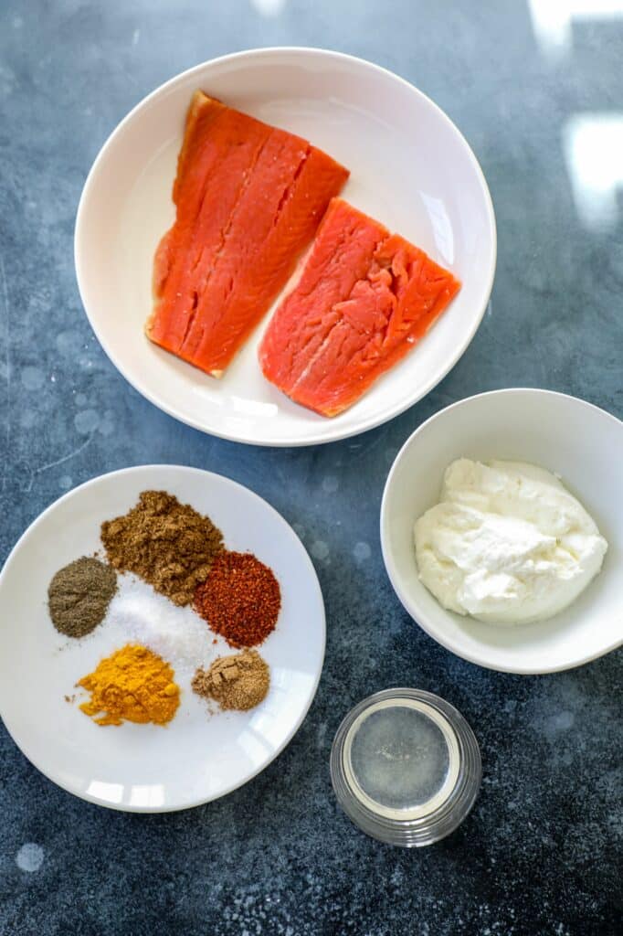 Ingredients needed for tandoori salmon on white plates.