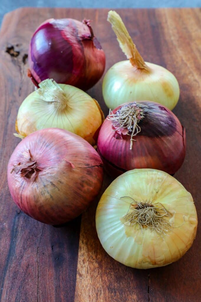 Red and yellow onions on a wooden cutting board.