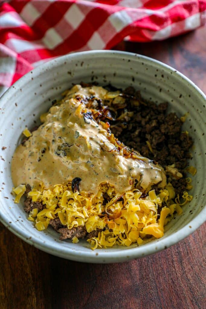 The ground beef, onions, and sauce mixed together in a bowl.