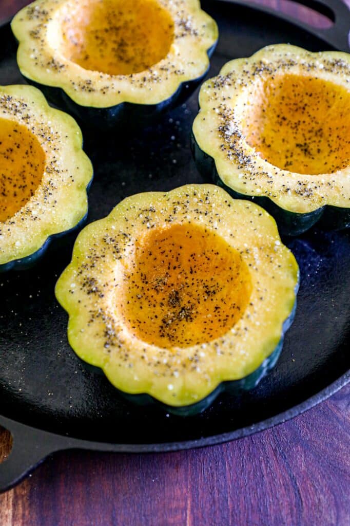 Sliced acorn squash halves, seasoned on a baking dish.