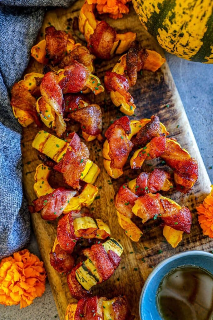 bacon wrapped delicata squash pieces that are on a cutting board