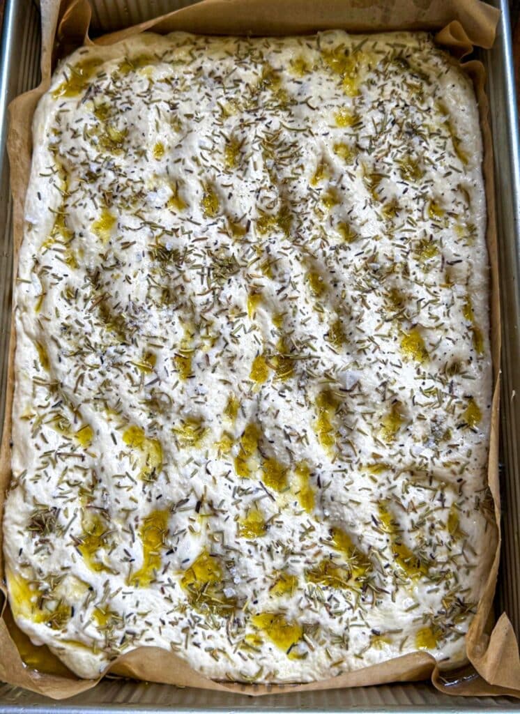 The dough dimpled and covered in rosemary and salt before baking